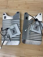 Two mini metal zydeco rubboards laid side by side, showing ridged surfaces and attached accessories including keys and leather thongs.