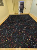 Full view of the large carpet displayed on the floor showing the complete multicoloured star and swirl pattern against a dark blue background.