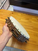 Side view of riq drum showing leather head and wooden inlay on frame with mounted cymbals.