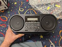 Front view of Sony ZS-RS60BT boombox showing speakers, control buttons, USB port, and LCD display.