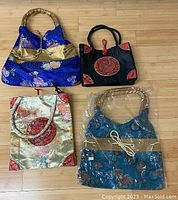 Four Thai silk purses featuring blue, black, gold, and blue-green colors with various embroidered floral and geometric designs, some with bamboo-style handles.