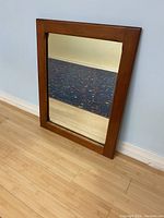 Front view of the vintage mahogany framed mirror showing the reflective surface and the warm brown color of the wood frame, standing on a hardwood floor against a wall.