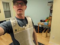Photo of a man wearing the handmade metal Zydeco washboard over his chest, showing the shape, ridges, and hammered texture around the neck area.
