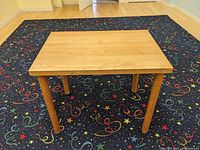 Front view of the rectangular wooden table showing the full table and legs on a patterned carpet.