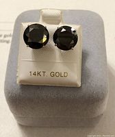 Two round black diamonds set in 14K white gold on a display stand marked ’14KT GOLD’.