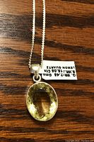 Close-up photo showing oval faceted lemon quartz stone set in sterling silver pendant, with chain and identification tag.