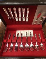 Full view of silverware set in red velvet-lined case showing knives, forks, spoons, and serving utensils.