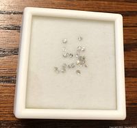 Loose diamonds displayed on a white cushioned surface inside a small white jewelry box.