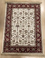 Full top view of the cream and red Persian-style rug with floral design and fringe, laid flat on the floor.