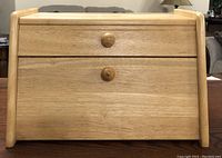 Front view of the maple wood bread box showing the closed roll-top lid, drawer, and bottom door with wooden knobs.