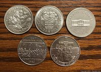 Five Canadian commemorative silver dollars displayed on a wooden surface, showing both sides in two photos. Coins feature detailed engravings representing Manitoba 1970, British Columbia 1971, PEI 1973, Constitution 1982, and Jacques Cartier 1984.