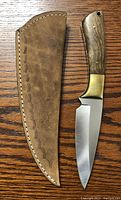 Top view of knife next to its tooled leather sheath, showing blade and handle details.