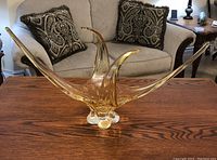 Amber art glass sculpture on wooden table, showing full wide view, organic shape with curved peaks.