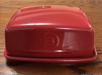 Red ceramic butter dish with cover and base set on wooden table, viewed from front.