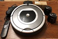 Photo of iRobot Roomba 780 vacuum cleaner with remote control, power adapter, and a box containing replacement battery or brushes