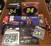 Photo of the Jeff Gordon NASCAR collectibles lot including ceramic mug in box, trailer hitch cover, key chain, and assorted decals