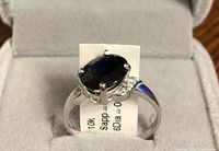 Front angled view of 10K white gold ring showing oval deep blue sapphire center and side diamonds