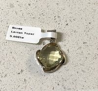 Photo of a cushion-cut lemon topaz pendant with a metal setting and attached label showing 5.80 carat weight.