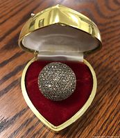 Top view of round dome-shaped sterling silver cocktail ring densely set with marcasite stones in heart-shaped gold-tone box with red velvet interior