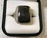 Top down view of sterling silver ring with dark iridescent rectangular stone sitting in white ring box