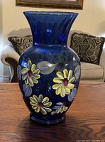 Photo of large cobalt blue glass vase with handpainted yellow flowers, placed on wooden surface in living area