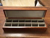 Full view of rectangular wooden box with open lid showing 12 compartments lined with grey velvet interior.