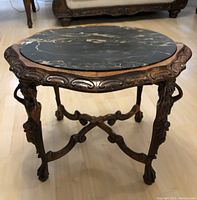 Full front view of the round table showing the black marble top with white veining and the carved wooden edge and legs.