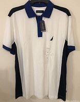 Front view of men's Nautica collared shirt in white with blue collar and black side panels, hanging on hanger, with tags attached.