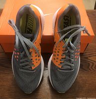 Top front view showing pair of grey and orange Nike running shoes with laces and orange box underneath