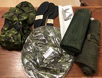 Photo of lot showing camo sun hat, ammo pouches, pairs of insoles, green mesh laundry bags, and folding cutting utensil on wooden table.