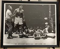 Framed black and white photograph showing Cassius Clay (Muhammad Ali) standing over Sonny Liston after a knockout in 1965. Referee Joe Walcott visible. Frame and glass intact.