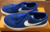 Pair of blue Nike SB Portmore 2 Ultralight shoes with white soles and swooshes displayed side by side on orange box.