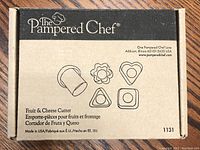 Box showing Pampered Chef Fruit & Cheese Cutter set with illustrated shapes on front: flower, heart, triangle, square cutter shapes.