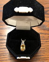 Front view of the sterling silver citrine pendant inside an octagonal black velvet jewelry box, showing the yellow citrine gemstone and diamond accents in the silver setting.