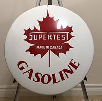 Photo of a large round metal advertising button sign featuring Supertest Gasoline logo with maple leaf and text