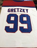 Back of white hockey jersey with red and blue trim showing large number 99 and name Gretzky with embroidered autograph.