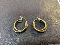 Photo showing pair of 10k gold double hoop earrings on a brown textured surface, highlighting twisted rope design.