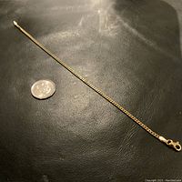 Full length of bracelet laid flat on black surface with a coin for scale