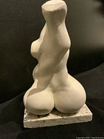 White abstract figural sculpture mounted on speckled granite base, front perspective.