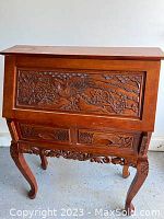 Front view of a medium wood-toned hand-carved cabinet/bar showing intricate carvings of birds and flowers on the front panel and drawers. Finished with cabriole legs and decorative carved apron.