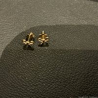 Pair of small 10K gold bow earrings photographed on textured black surface, showing front and side views, highlighting shape and condition.