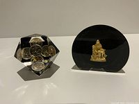 Front view of two lucite paperweights: one faceted containing coins, the other smooth with a statue inside.