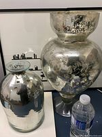 Pair of mercury glass vessels, showing full height and reflective surface with mottled aged silver finish.