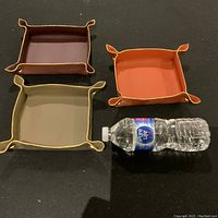 Three handmade Italian leather valet trays arranged side by side with a water bottle for size comparison, showing colors and shape.