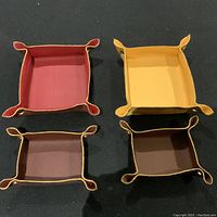 Four handmade Italian leather valet trays in different colors arranged on a dark surface, showing overall view of the lot.