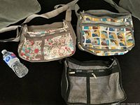 Three vintage LE SPORTSAC handbags displayed together on a dark surface alongside a water bottle for scale, showing different fabric patterns and front zipper pockets.