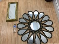 Both mirrors laid flat on hardwood floor with water bottle for scale