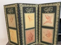 View showing all three panels of the vintage folding screen with framed sketches and painted gold borders.