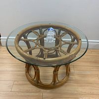 Full view of the round rattan table with the circular glass top holding a water bottle demonstrating size and surface detail.