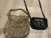 Both handbags displayed side by side on a wooden floor, beige one with chain and flap, black one with zip pocket and strap.